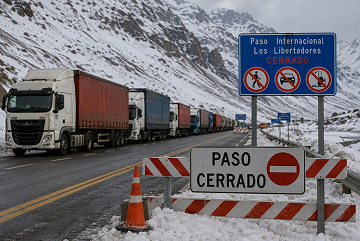 Fila de camiones detenidos al costado de la ruta internacional en zona cordillerana, con nieve acumulada en la banquina y señalización de paso cerrado
